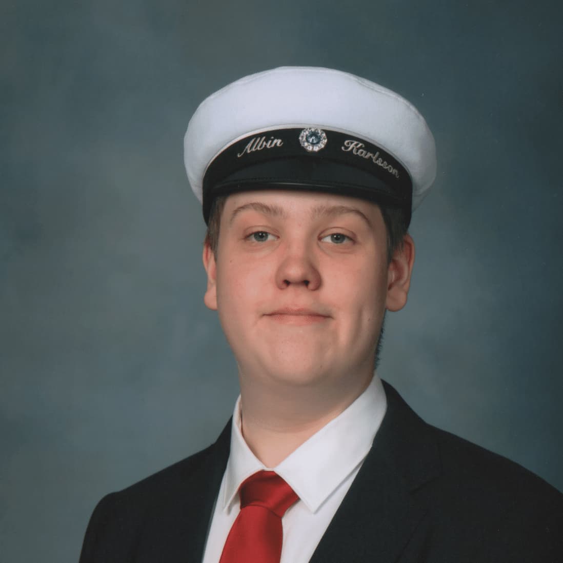 Portrait of a young man wearing a student cap and a black suit with a red tie.